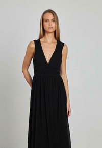 Schwarzes Maxikleid mit tiefem V-Ausschnitt, strukturierten vertikalen Falten und tailliertem Bund. Mit breiten Trägern und einem schwingenden Rock.