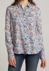 Camicia a bottoni floreale in tessuto leggero con un motivo floreale multicolore in tonalità di blu, pesca e verde. Include bottoni neri e maniche lunghe.