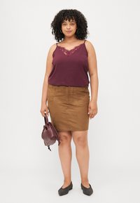 Burgundy lace-trimmed tank top, brown suede skirt, and black flats. Holding a maroon handbag with a rounded design.