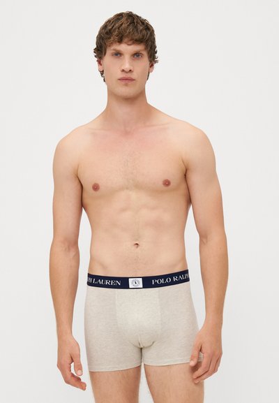 Boxeri gri din material moale, cu un talie de culoare bleumarin pe care este inscripționat "Polo Ralph Lauren." Designul este ajustat, iar modelul stă drept.