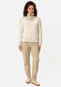 Light beige fleece jacket with a high collar and zip closure, paired with beige trousers and light shoes. Smooth texture, minimal detailing.