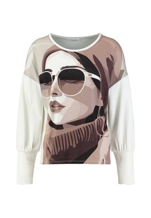 Camicia bianca a maniche lunghe con una grande grafica stampata di una donna che indossa occhiali da sole, un foulard e un maglione a coste con collo alto.