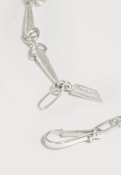 Ασημένιο κολιέ με αλυσίδα με επιμηκυσμένους κρίκους και μια μικρή πλακέτα με χαραγμένο το όνομα "loren stewart" σε λευκό φόντο.