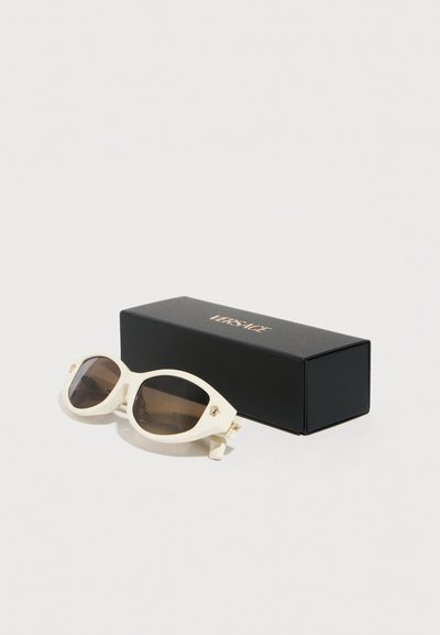 Λευκά οβάλ γυαλιά ηλίου με σκούρους φακούς και χρυσό λογότυπο Μέδουσας στις αρθρώσεις, δίπλα σε μαύρη θήκη με την επωνυμία Versace, σε λευκό φόντο.