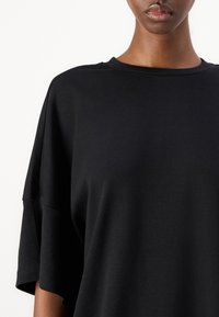 Tricou oversized negru cu guler rotund și mâneci scurte. Fabricat dintr-un material moale cu o textură fină și un design minimalistic.