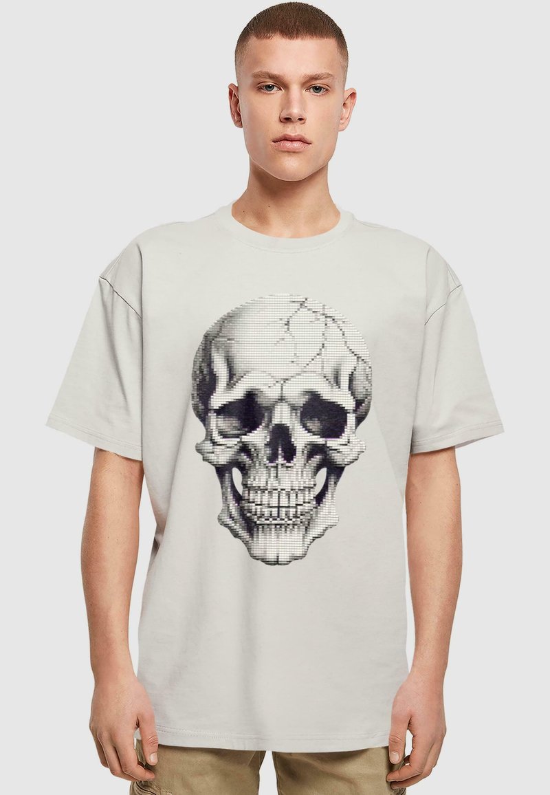 Lys grå kortærmet t-shirt med et stort sort-hvidt skull grafik i et pixeleret design med revnede detaljer.