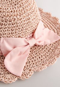 Chapeau de paille rose pâle avec un large bord, présentant un design tissé texturé et un grand nœud en tissu rose à la base en guise d'accent.