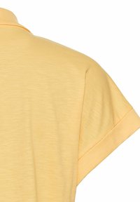 Poloshirt i lys gul, kortærmet med foldet manchet. Blødt, tekstureret stof med en let glans og et klassisk kravedesign.