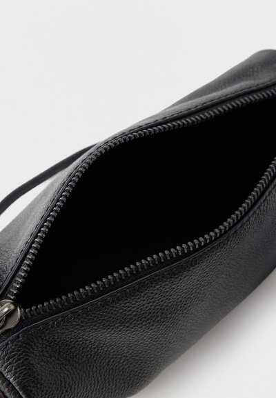 Μαύρο υφασμάτινο δερμάτινο πορτοφόλι με ανοιχτό φερμουάρ που δείχνει ένα άδειο εσωτερικό, από ψηλά σε λευκό φόντο.