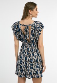 Rochie cu model, caracterizată prin mâneci volan, închidere cu fundă pe spate și o combinație de culori bleu, bej și negru cu un design floral.