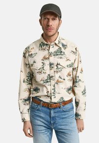 Langärmliges Hemd in Creme mit einem naturinspirierten Druck, der Bäume, Tiere und Landschaften zeigt. Das Material scheint aus Baumwolle zu sein.