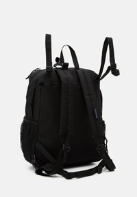 Sac à dos noir fabriqué à partir d'un tissu résistant, doté de bretelles rembourrées, d'une poche latérale en maille et d'une poignée supérieure pour un transport facile.