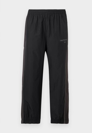 Pantaloni negri sportivi cu talie și mansete elastice, având dungi laterale și un mic logo New Balance pe partea superioară a coapsei stângi.