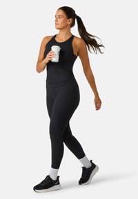 Svart ribbad linne topp parat med svarta leggings, bärs med svarta sneakers och vita ankelsockor, håller en kaffekopp, går.