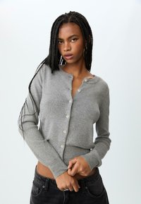 Grijze gebreide cardigan met een knoopsluiting aan de voorkant, lange mouwen en een geribd textuur. Heeft een ronde halslijn en kleine, lichtgekleurde knopen.