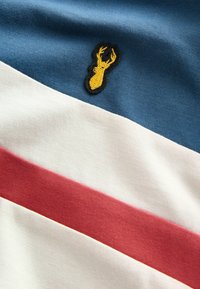 Cămașă din bumbac cu mânecă scurtă, având dungi orizontale în nuanțe de albastru, alb și roșu, cu un logo de homar brodat în galben pe secțiunea albastră.