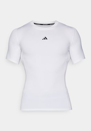 Chemise blanche à manches courtes en tissu technique, avec un col rond et un logo noir sur la poitrine. Texture lisse et design ajusté.