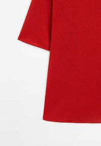 Haut en coton rouge à manches courtes, avec une texture lisse et une coupe décontractée. L'ourlet est droit et net, sans accents visibles.