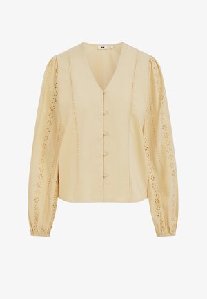 Bēša blūze ar V-veida izgriezumu, gariem piedurknēm, pogu aizdari un dekoratīvām izšuvumiem uz piedurknēm un priekšpusē. Izgatavota no viegla auduma.