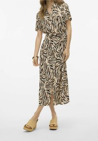 Robe imprimée animalière en beige clair avec des rayures noires et brunes, à manches courtes et avec une fente devant. Associée à des sandales à plateforme beiges.