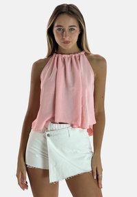 Top halter rosa de tela ligera, con escote fruncido y un diseño fluido, combinado con pantalones cortos blancos con bordes desflecados.