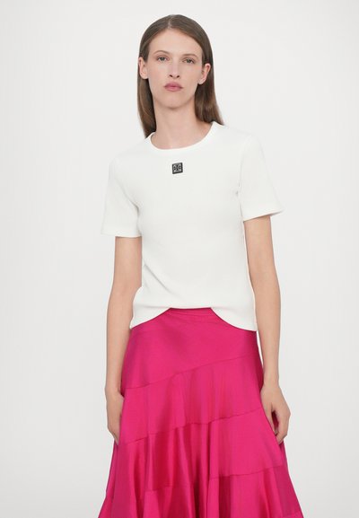 Haut blanc à manches courtes côtelé avec un col rond et un détail logo noir ; assorti à une jupe longue rose en couches.
