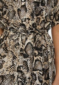 Abito camicia con bottoni caratterizzato da un motivo a serpente multicolore in beige, nero e marrone, dotato di una cintura in tessuto e gonna plissettata.