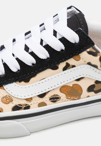 Sneaker mit Leopardenmuster, ausgestattet mit einem beigen Canvas-Obermaterial und schwarzen Wildlederelementen, einem weißen Markenstreifen und weißen Schnürsenkeln. Gummisohle.