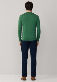 Grüner, leichter Pullover mit langen Ärmeln und rundem Ausschnitt, kombiniert mit dunkelblauen Hosen und braunen Schuhen. Keine sichtbaren Muster.