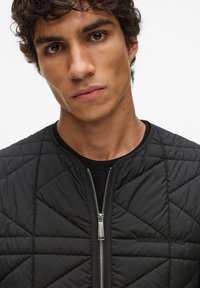 Zwarte doorgestikte bomberjas met een ritssluiting aan de voorkant, een geribde kraag en een geborduurd logodetail. Heeft een diamantpatroon en een gladde textuur.