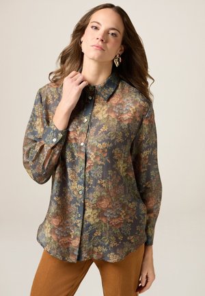 Camisa de botón floral en tejido transparente, con tonos de marino, naranja y verde, con cuello clásico y mangas largas.