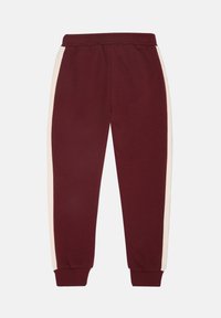 Bordeauxrode trainingsbroek met crèmekleurige zijstrepen, een elastische Tailleband en geribde boorden. Gemaakt van zacht materiaal met een gladde textuur.