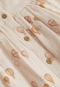 Lys beige stof med et mønster af pastelfarvede luftballoner og skyer. Indeholder to brune knapper på den frontplettede design.