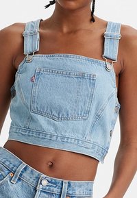 Ljusblå denimoverall med korta ben, justerbara axelremmar, framficka och metalldetaljer. Slät textur och avslappnad design.