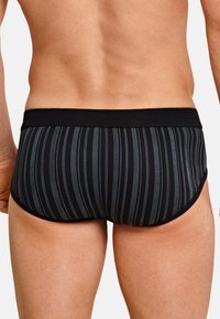 Schwarze Badebriefe mit vertikalen blauen Streifen, ausgestattet mit einem kontrastierenden schwarzen Bund und einem figurbetonten Design, das sich dem Körper anpasst.