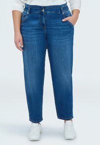 Jean en denim bleu moyen, taille haute avec une coupe droite. Doté de poches latérales, de légers effets usés et d'une fermeture à bouton et fermeture éclair.