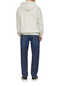 Sweatshirt à capuche gris clair avec une coupe ample, associé à un jean en denim bleu foncé avec deux poches arrière et des accents de couture jaune.