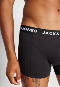 Schwarze Baumwoll-Boxershorts mit einem schwarzen Bündchen, auf dem der weiße Text "JACK & JONES" zu sehen ist. Sichtbare Nähdetails und passgenaues Design.