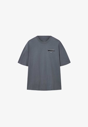Šedé tričko s krátkym rukávom vyrobené z bavlny. Obsahuje čierny obdĺžnikový potlačený štítok na ľavej strane hrudi s názvom značky a logom.