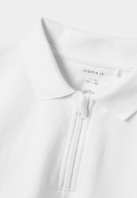 Vit polo-shirt med dragkedja och kort krage, tillverkad av texturerat tyg. Storleksmärke synligt: 7-8 år, 122-128 cm.
