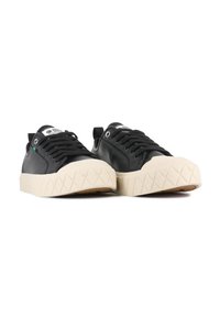 Sneaker nere in pelle con suola piatta in crema testurizzata, dotate di lacci neri, etichetta con logo e un accento verde vicino ai fori dei lacci.
