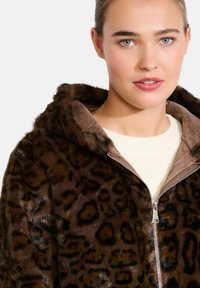 Hnedá umelá kožušina s leopardím vzorom, so zipsom a kapucňou. Má mäkkú vnútornú podšívku vo svetlejšom hnedom odtieni.
