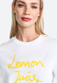 White t-shirt featuring a yellow handwritten "Lemon Juice" graphic. The fabric is cotton, with a round neckline and short sleeves.