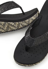 Black flip-flops with textured black straps and a patterned outsole featuring black, white, and beige. Lightweight with a cushioned footbed.