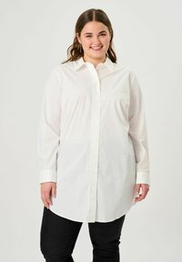 White long-sleeve button-up shirt with a collar, featuring a straight cut and soft fabric. Paired with black fitted pants.