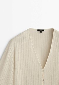 Beige geribde cardigan met een V-hals en korte mouwen. Voorzien van een knoopsluiting aan de voorkant. Zachte textuur en lichtgewicht materiaal.