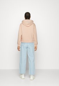 Lichtroze cropped hoodie met een capuchon, gecombineerd met lichtblauwe wijde jeans. Witte sneakers maken de casual outfit compleet.