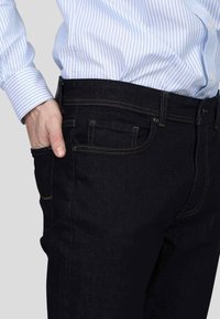 Jeans en denim bleu foncé avec un design ajusté, dotés de cinq poches et de coutures jaunes contrastantes le long des coutures et des poches.