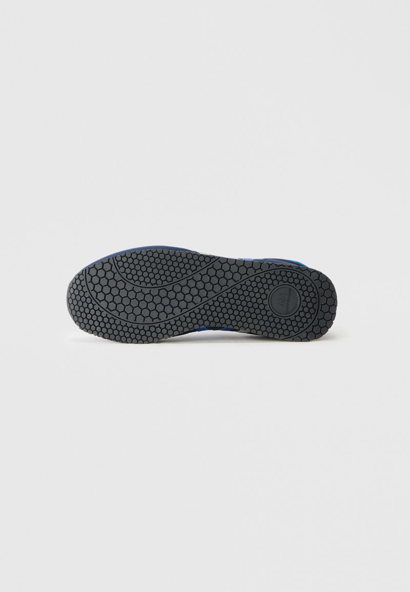 Suela de zapato de goma negra con un patrón texturizado en forma de panal y surcos curvados; destaca los elementos de diseño de durabilidad y tracción.