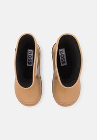Bottines beige avec une finition brillante, doublure intérieure noire et semelle flexible. Présente un logo "BOSS" sur l'étiquette intérieure.